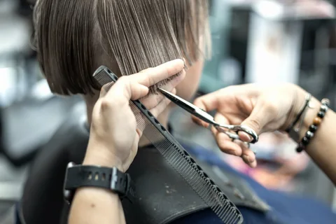 Coiffeuse beim Haarschnitt mit Schere und Kamm.